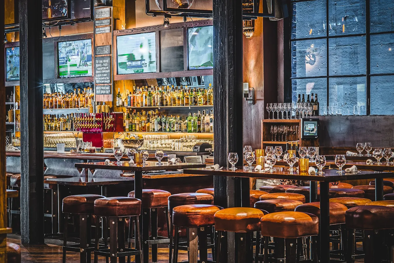 Photo of a bar with dark lighting, leather barstools, and drinks