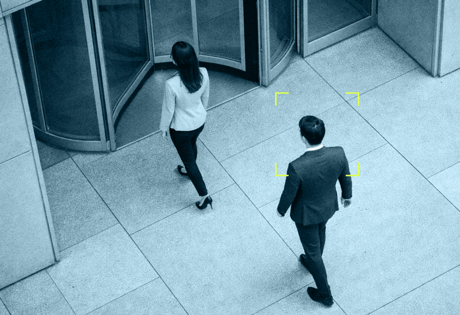 Man following woman into corporate office building, camera looking down on them walking
